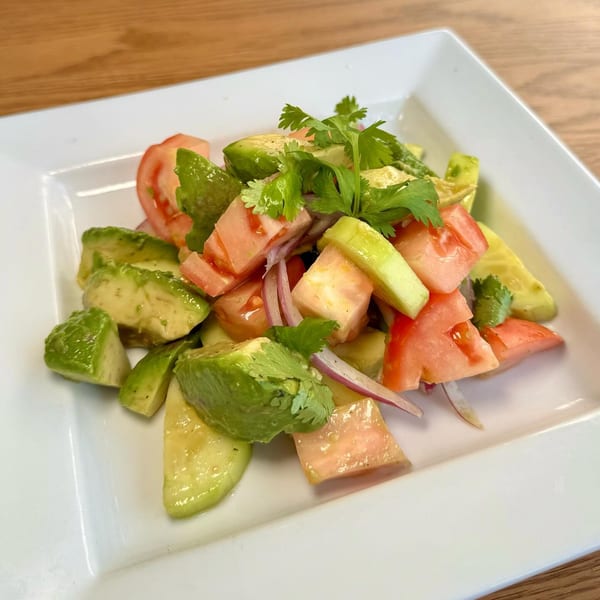 A vibrant Italian salad with diced avocado, tomatoes, red onion, and fresh cilantro on a white plate.