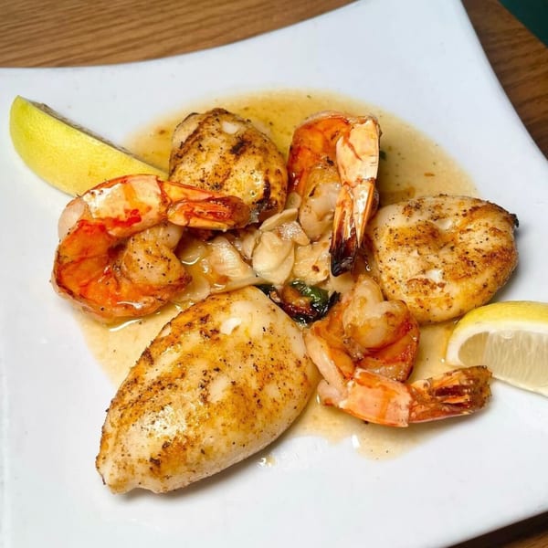 Grilled shrimp and scallops with lemon wedges and sauce on a white plate at Villaggio Ristorante.