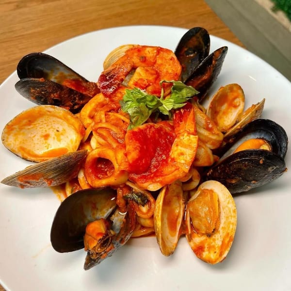 A vibrant seafood pasta dish with mussels, clams, shrimp, and squid in red sauce, garnished with basil.