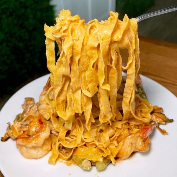 Fork lifting creamy fettuccine pasta with shrimp and mussels from a white plate.